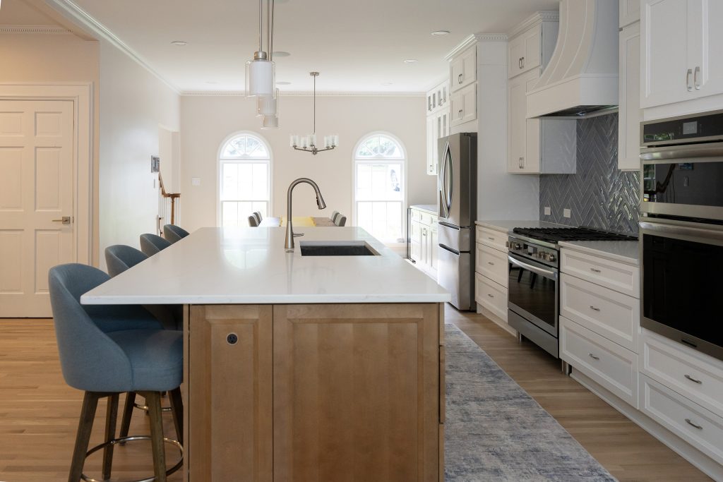 Long view down the island toward arched windows, with the range wall and wall ovens to the right.