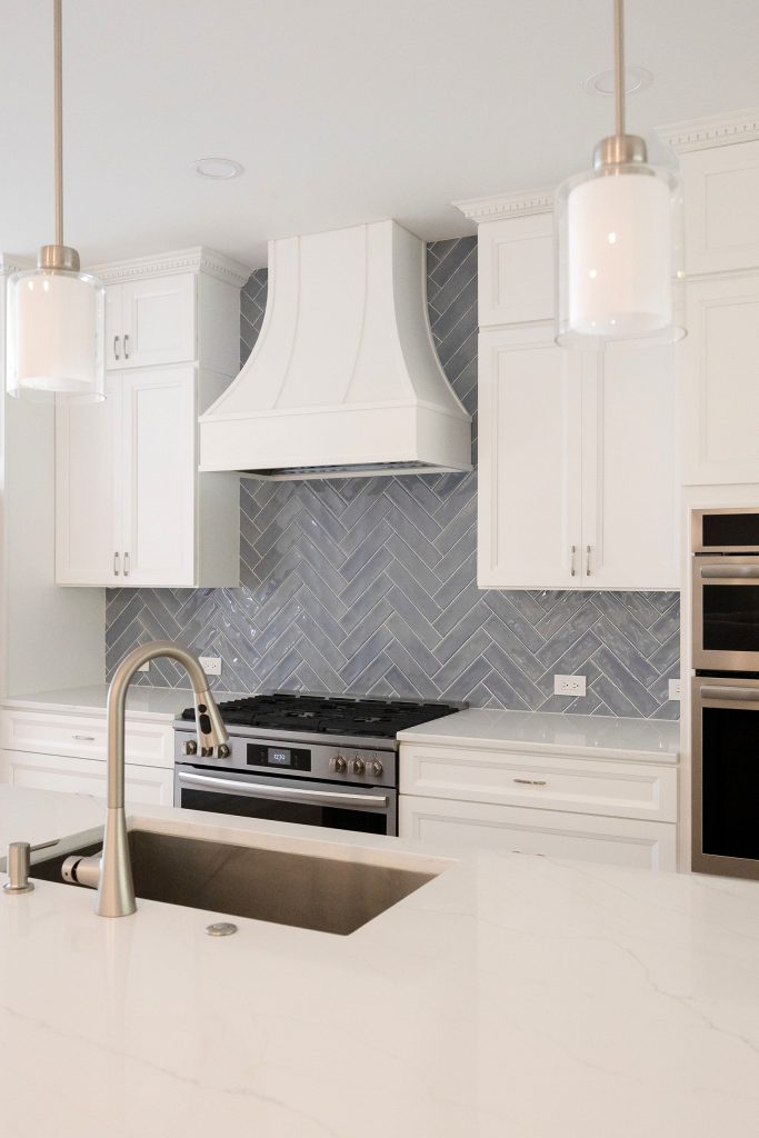Island sink and brushed nickel faucet with the range, custom hood and wall ovens beyond.