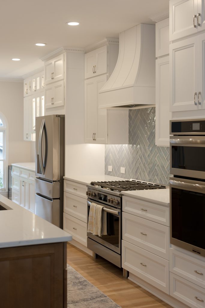 View past the stainless refrigerator to the range and custom hood, with dentil crown molding and white oak flooring.