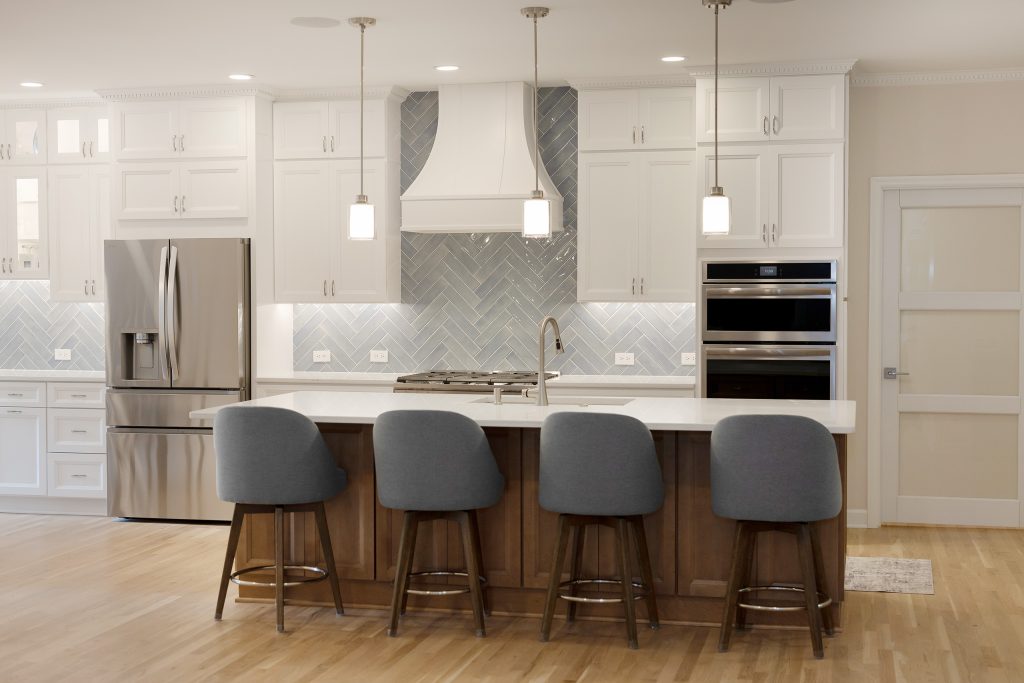 Kitchen viewed from the family room, with the island, four counter stools, double wall ovens and a frosted glass door to the pantry.
