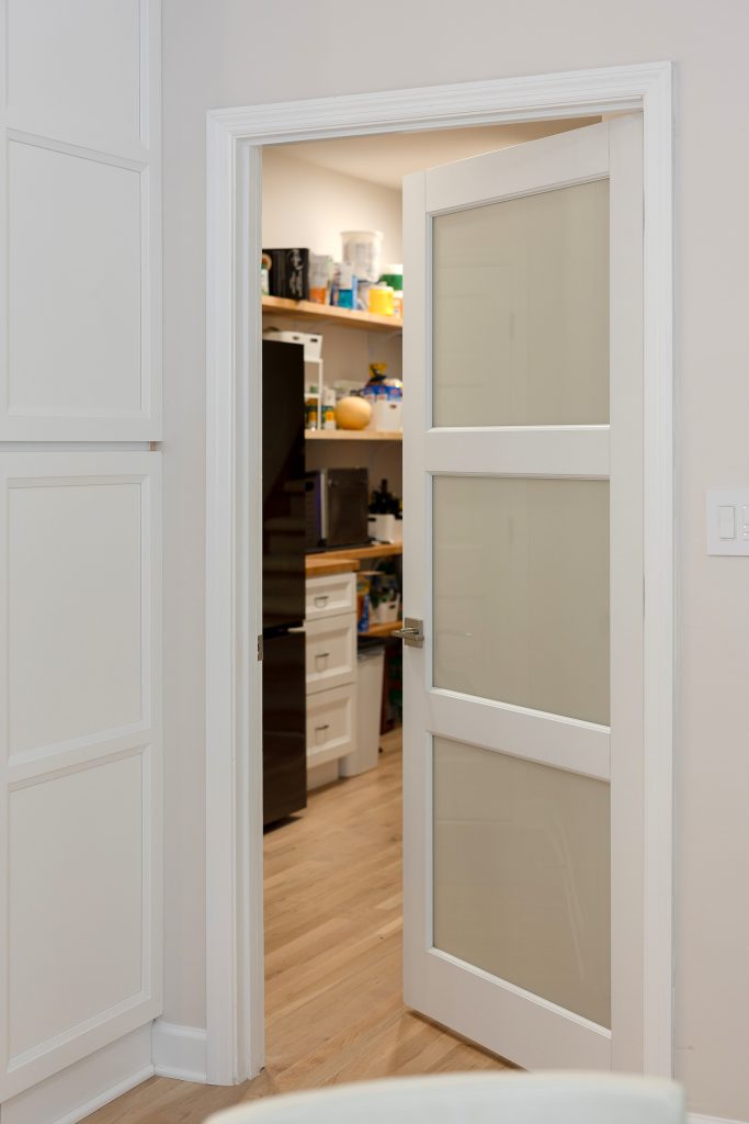 Walk-in pantry behind a frosted three-panel glass door, fitted with butcher block shelving over white oak flooring.