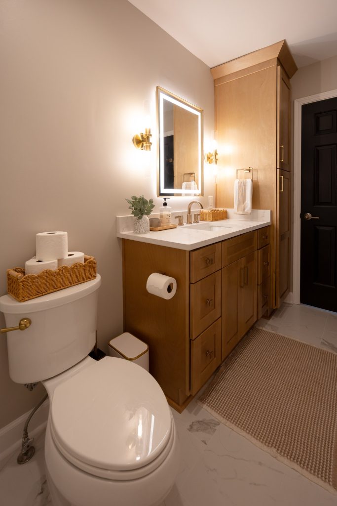 Maple vanity and linen tower with brass hardware, seen past the toilet toward the bathroom door.