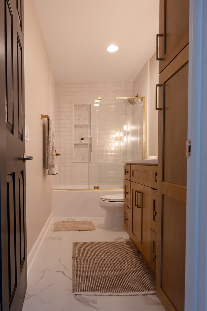 View into the bathroom from the doorway, with the glass-enclosed tub, tiled niche and maple vanity.