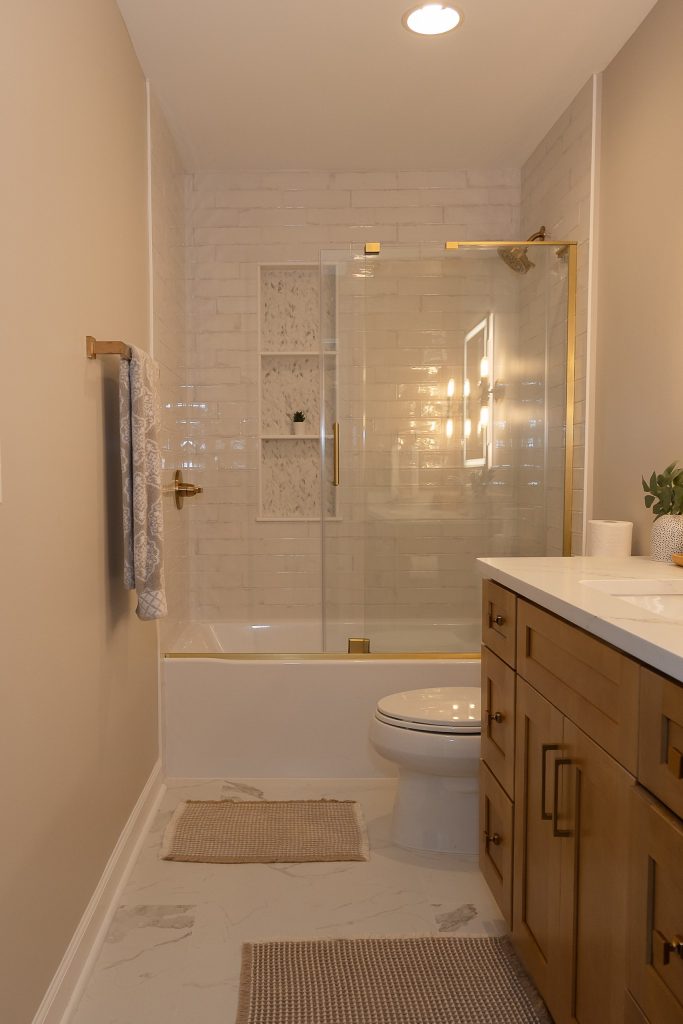 Bathroom with a tub behind a brass-framed glass enclosure, a chevron marble niche and marble-look porcelain flooring.