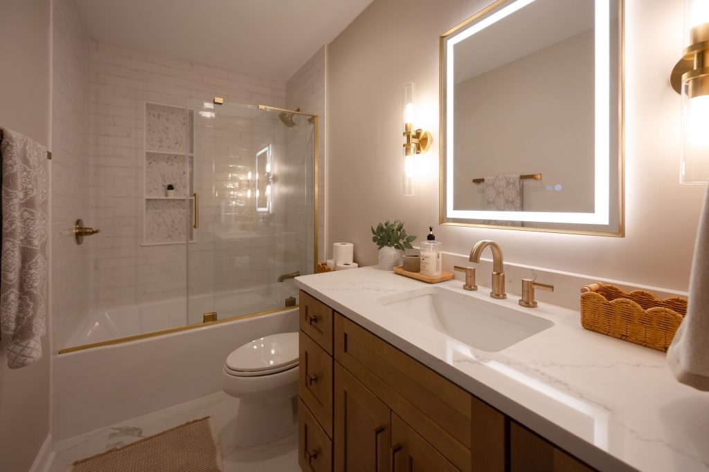 Wide view of the bathroom showing the tiled tub surround, chevron marble niche, quartz vanity and brass fittings.